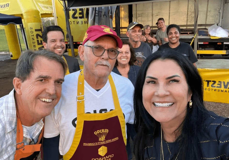Group of people smiling and taking a selfie at an outdoor event with yellow banners in the background.