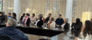 Group of people sitting at conference table in a room with beige curtains.