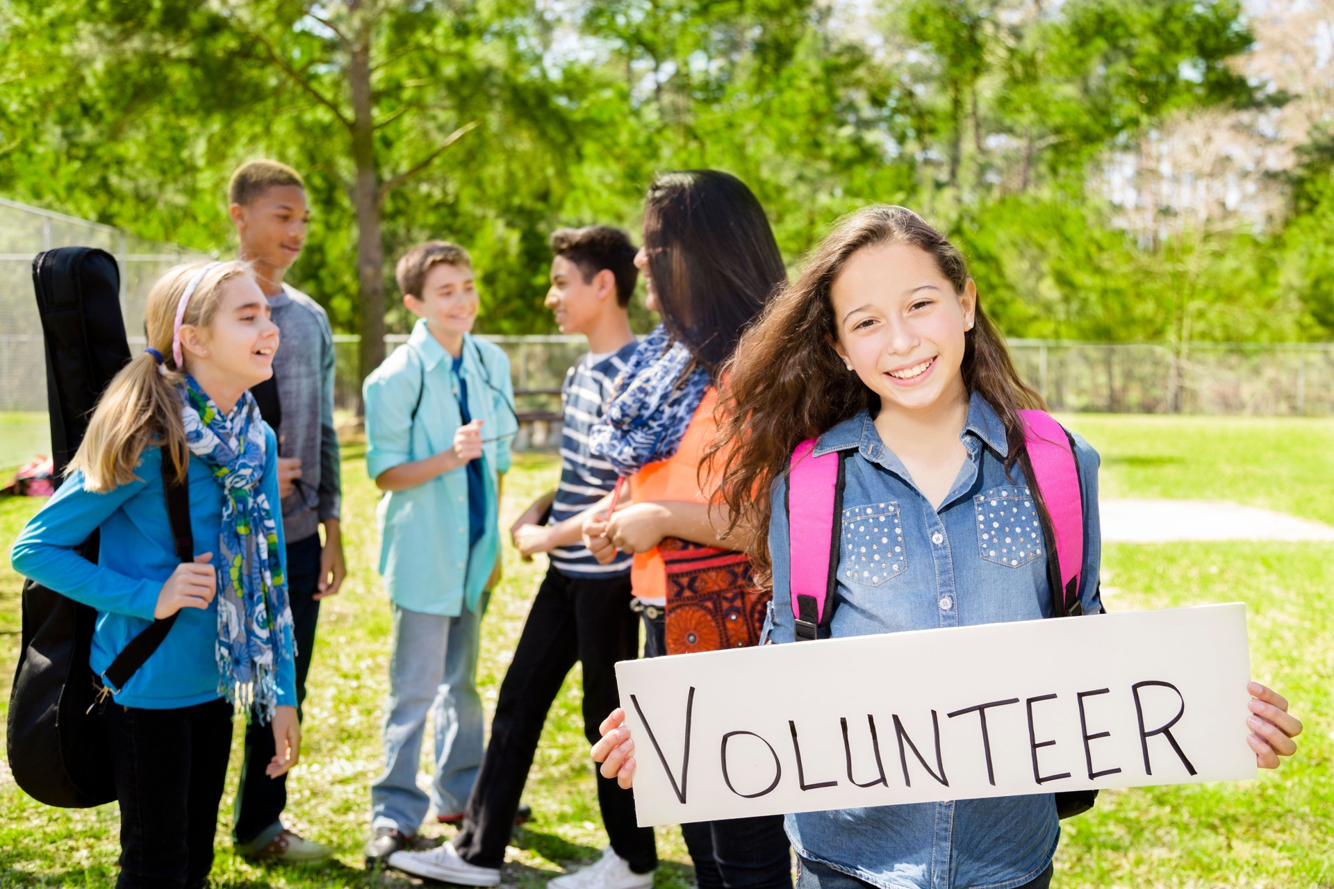 Teenagers: Latin girl holds "Volunteer" sign. Group of friends.